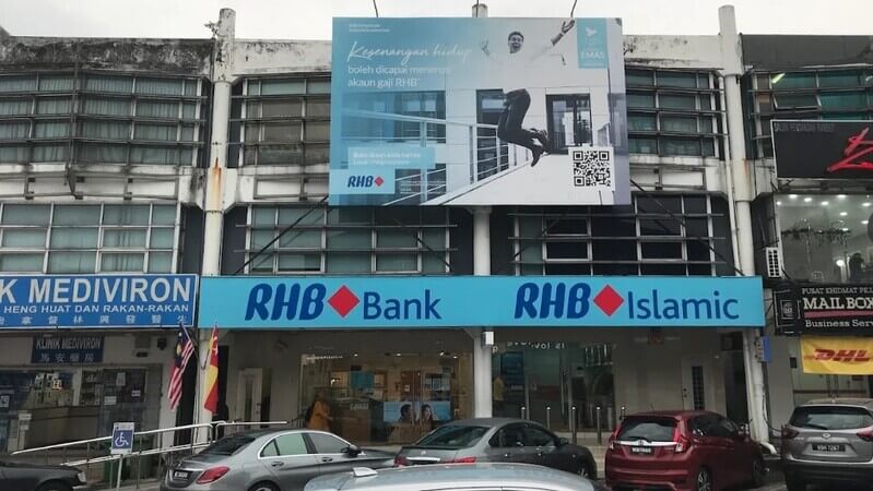 Pandangan hadapan bangunan lot kedai yang memaparkan papan tanda cawangan RHB Bank UEP Subang Jayadan RHB Islamic, dengan papan iklan promosi besar di tingkat atas serta beberapa kenderaan yang diletakkan di ruang parkir hadapan