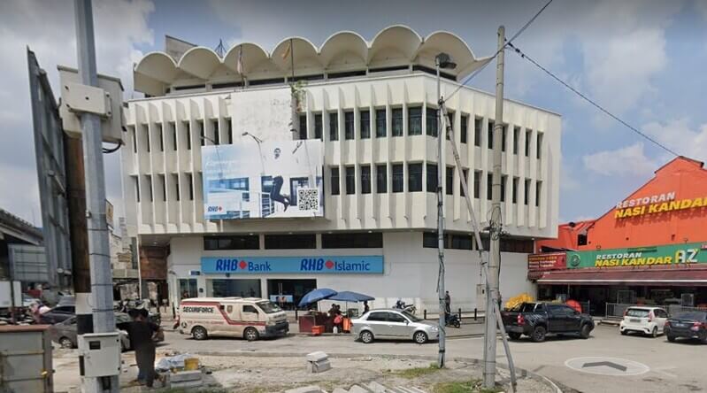 Pemandangan luar bangunan cawangan RHB Bank dan RHB Islamic bertingkat di tepi jalan raya. Di sebelah kanan bangunan bank, terdapat Restoran Nasi Kandar AZ berprestij berwarna jingga, manakala di bahagian hadapan kelihatan kenderaan yang diletakkan dan lalu-lalang,