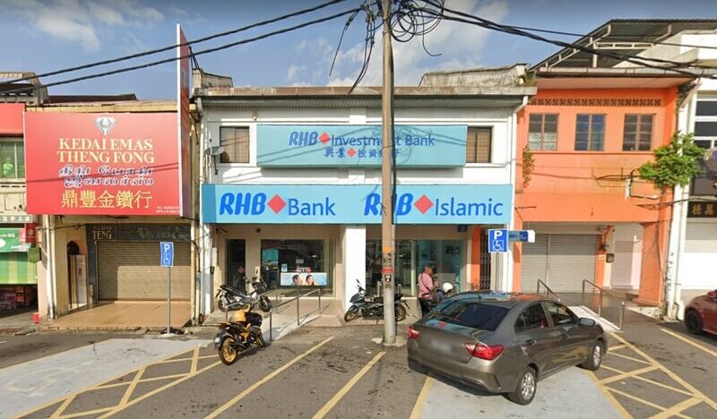 Pandangan hadapan bangunan dua tingkat cawangan RHB Bank dan RHB Islamic dengan papan tanda RHB Investment Bank di tingkat atas. Terdapat tempat letak kereta di hadapan premis, sebuah kereta sedan kelabu, beberapa motosikal, serta papan tanda kedai emas