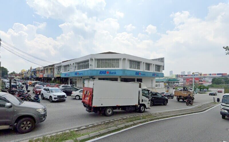 Pandangan luar cawangan RHB Bank Taman Taming Jaya di kawasan rumah kedai dengan kenderaan diletakkan di hadapan dan lori putih melintas di jalan raya